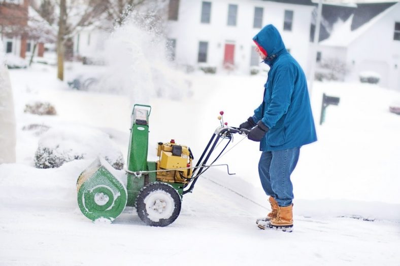 Man in a blue jacket with a snow blower
