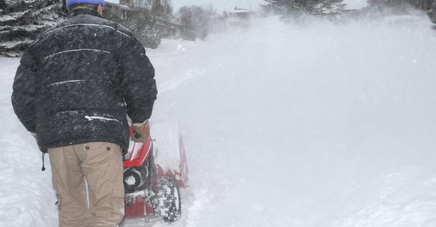 Man clearing snow with a red snowplow